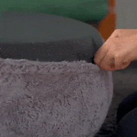 Personne ajustant le rembourrage d'un lit pour animaux Comfy Wopiloo en peluche grise.